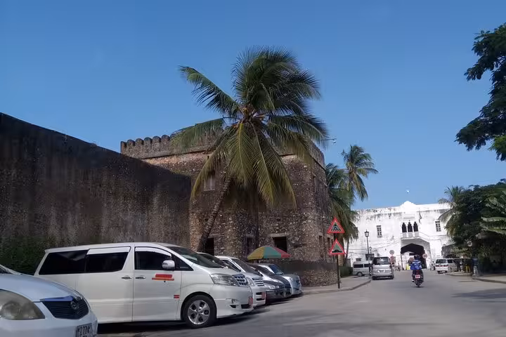 White minivans parked near historical buildings in Zanzibar, ideal for private airport transfers to hotels.