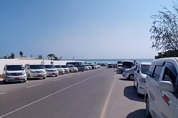 Long line of transfer vehicles at Zanzibar Airport, providing seamless hotel transfers with ocean view backdrop.