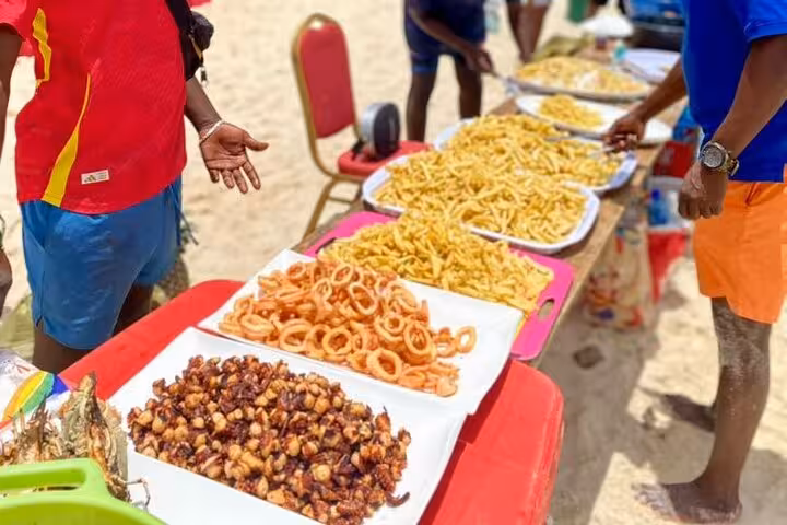 Beachside food stall in Zanzibar offering a variety of local fried delicacies and snacks on colorful trays.