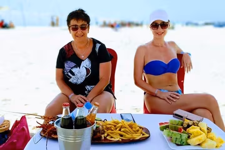 Tourists enjoying fresh seafood and tropical fruits on a pristine Zanzibar beach, ideal for a culinary adventure.