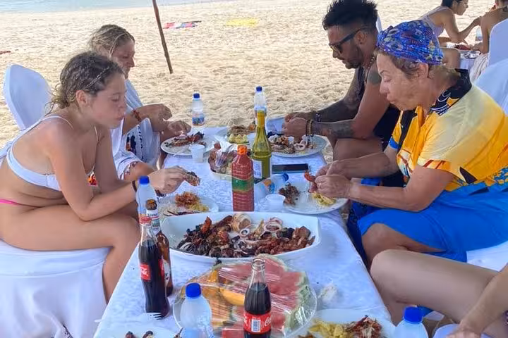 Group enjoying a seafood feast at a beachside table in Zanzibar, surrounded by sand and ocean views.