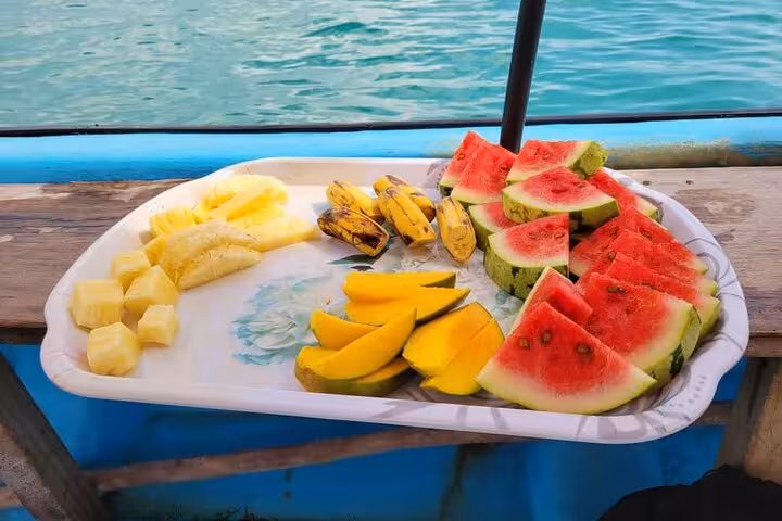 A vibrant platter of tropical fruits served on a boat in Zanzibar, showcasing exotic flavors against a turquoise sea backdrop.