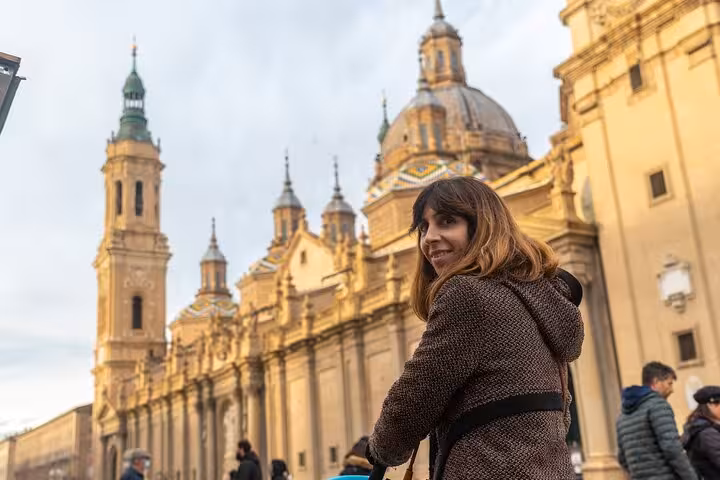 A smiling woman stands in front of the stunning Basilica de Nuestra Señora del Pilar during a Zaragoza city walk.