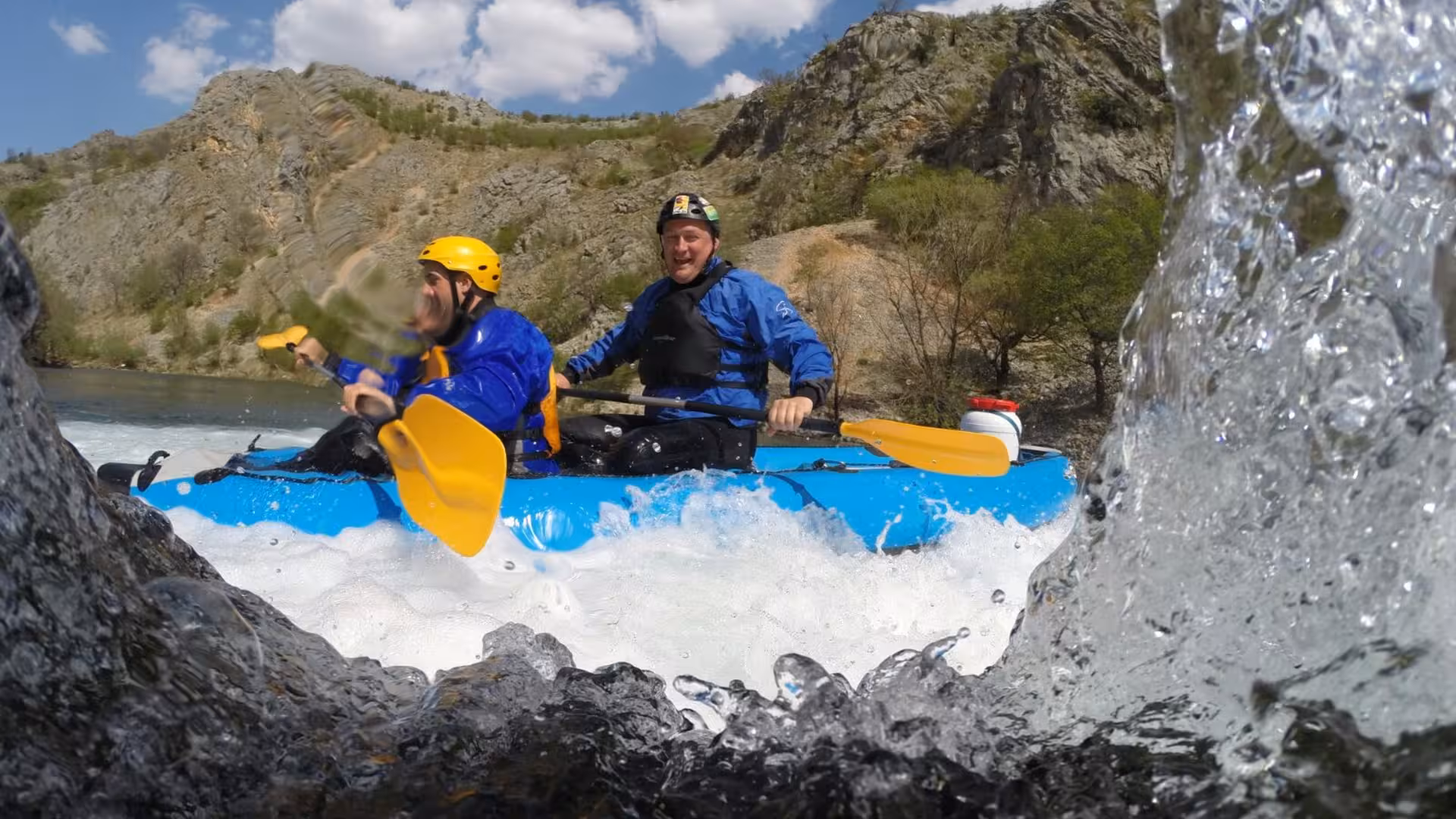 Two kayakers paddling and water splashing in the camera