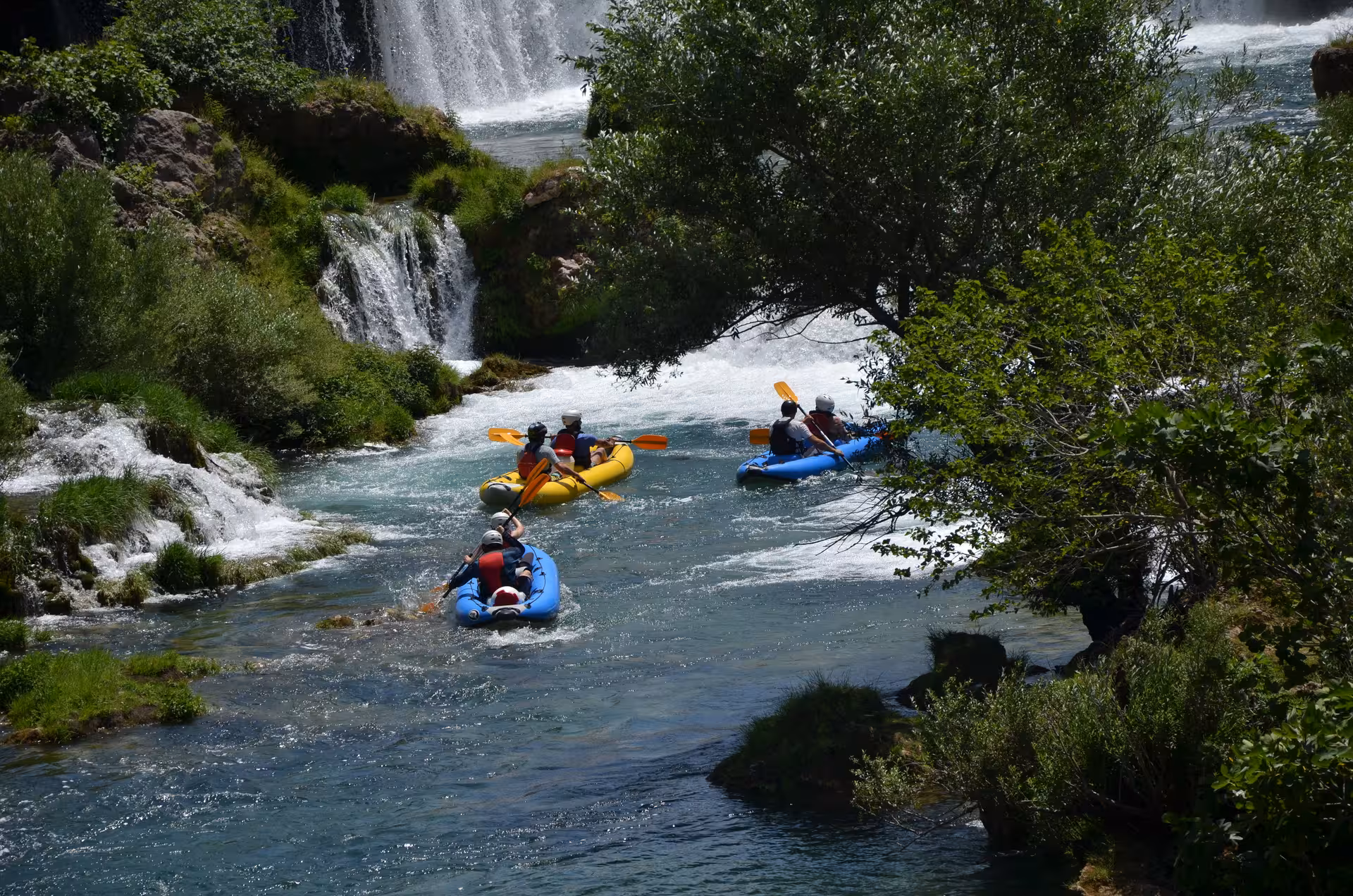 Canoeists paddling through serene Zrmanja River with waterfalls and lush landscapes in the background.