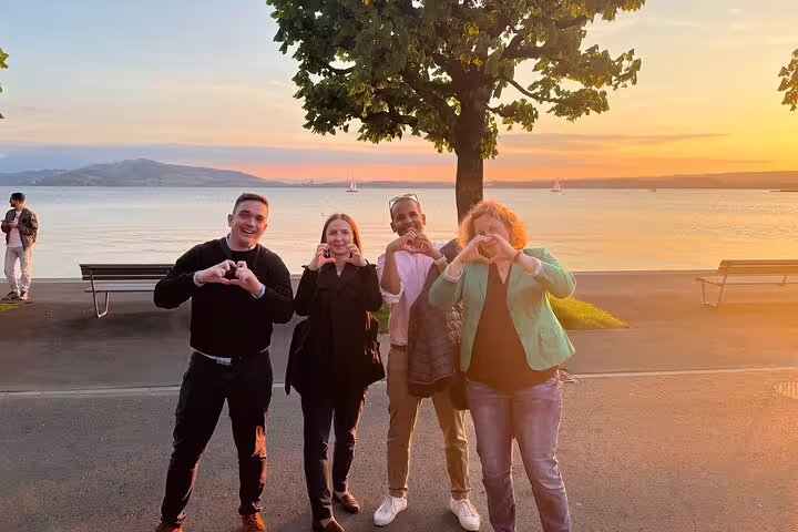 Group making heart signs at sunset on Lake Zug promenade during a Zug self-guided scavenger hunt tour