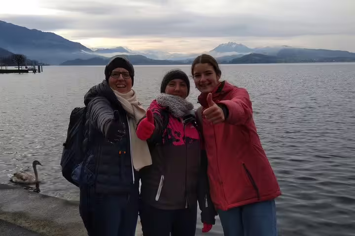 Friends posing by Lake Zug waterfront during Zug scavenger hunt self-guided tour with alpine views behind