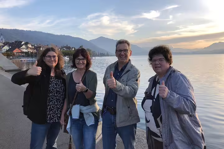 Friends giving thumbs up on Zug lakeside promenade at sunset during a self-guided Zug scavenger hunt tour