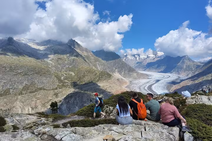 Hikers resting on alpine rocks overlooking the Aletsch Glacier on a Zurich day trip in the Swiss Alps