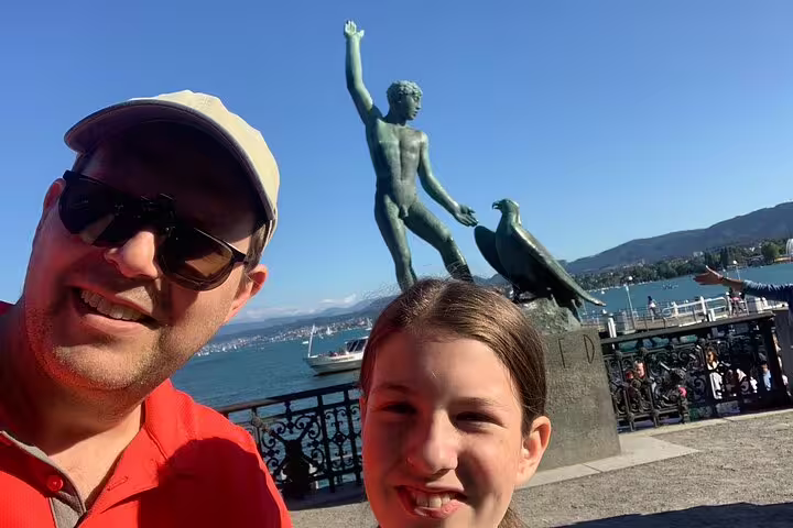 Family selfie at Zurich Bürkliplatz Ganymede statue with Lake Zurich views on a self-guided scavenger hunt