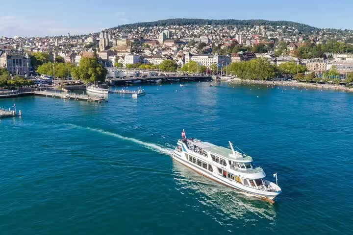 A scenic view of a boat cruising on Lake Zurich with the picturesque city skyline in the background.
