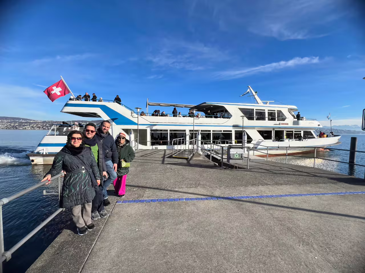Tourists enjoying a scenic cruise on Lake Zurich with Swiss flag and boat under a clear blue sky.