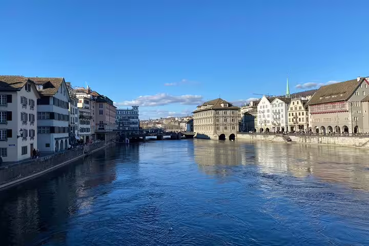 Scenic view of Zurich's historic buildings lining the tranquil Lake of Zurich under a clear blue sky.