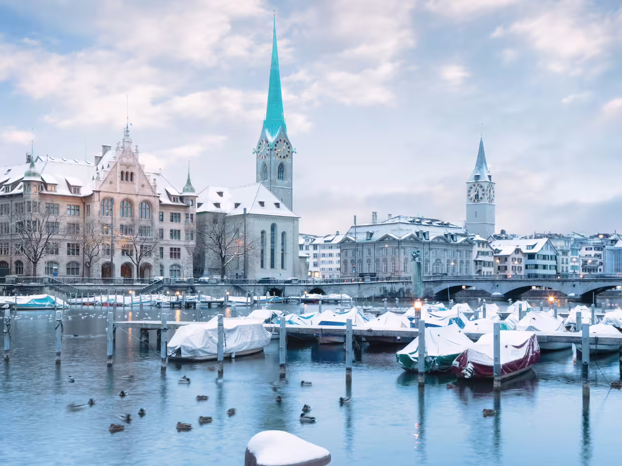 Snow-covered boats and historic architecture along the Limmat River in Zurich during winter on a private tour.