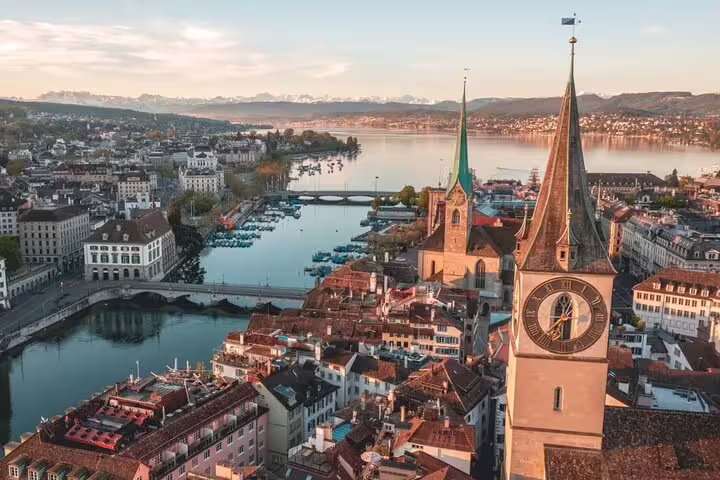 Aerial view of Zurich's historic old town with iconic church towers and serene lake in the background at sunset.