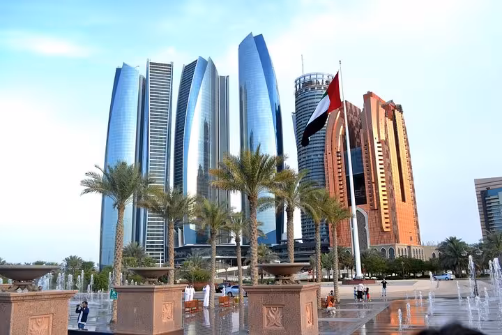 Modern skyscrapers and UAE flag amidst palm trees in Abu Dhabi, highlighting cityscape for desert safari tour.