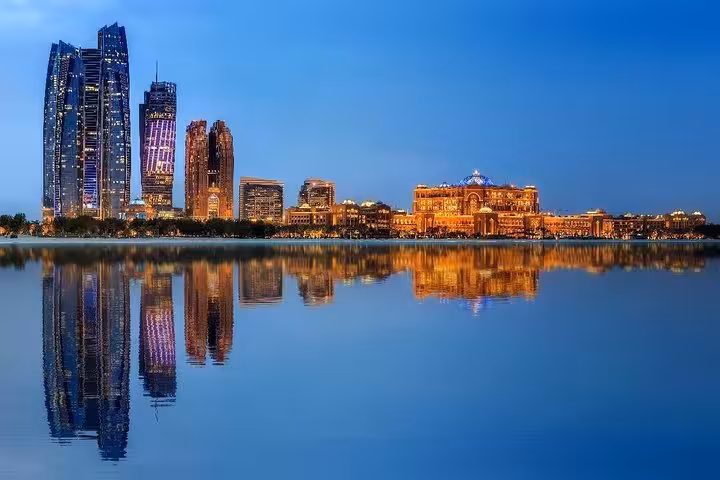 Abu Dhabi skyline with illuminated skyscrapers reflecting on water during twilight, featured in city tour.