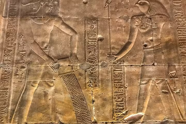 Ancient Egyptian wall relief with hieroglyphs at Aswan temple, seen on Luxor to Abu Simbel tour