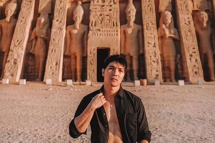 Visitor posing at Abu Simbel entrance on a full-day guided tour from Aswan, with carved pharaoh columns