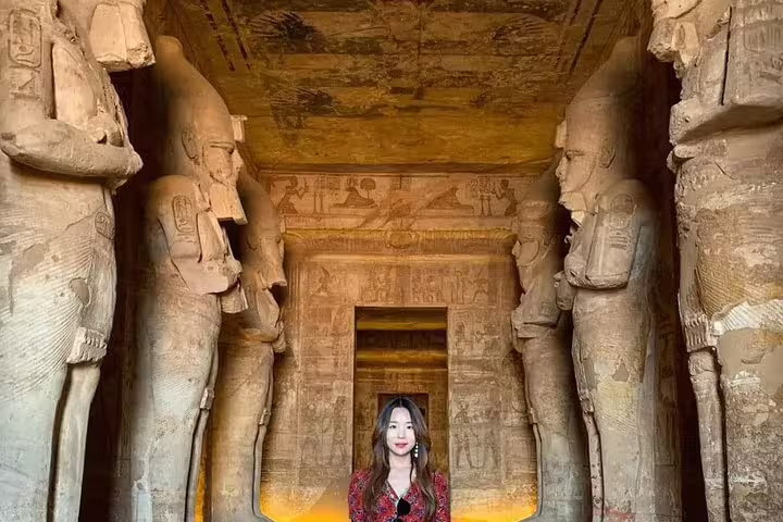 Traveler inside Abu Simbel temple hall between colossal statues, guided day trip to Abu Simbel from Aswan