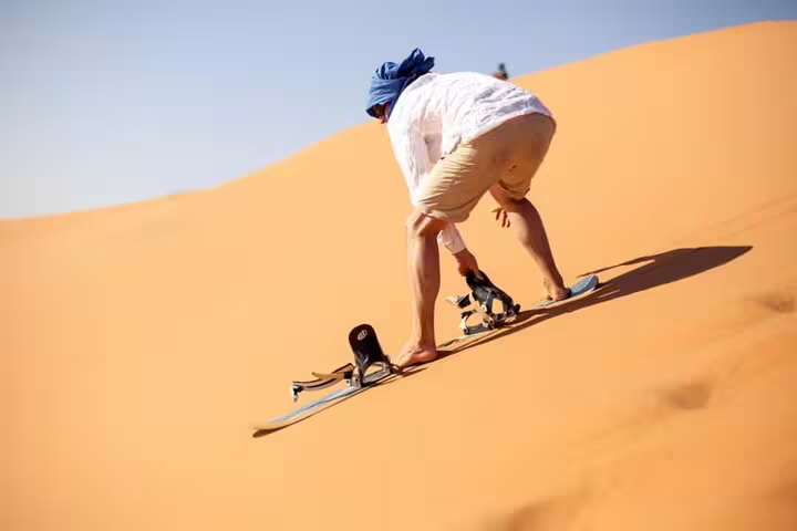 Adventurer sandboarding down a sunlit desert dune during an exhilarating desert safari experience.