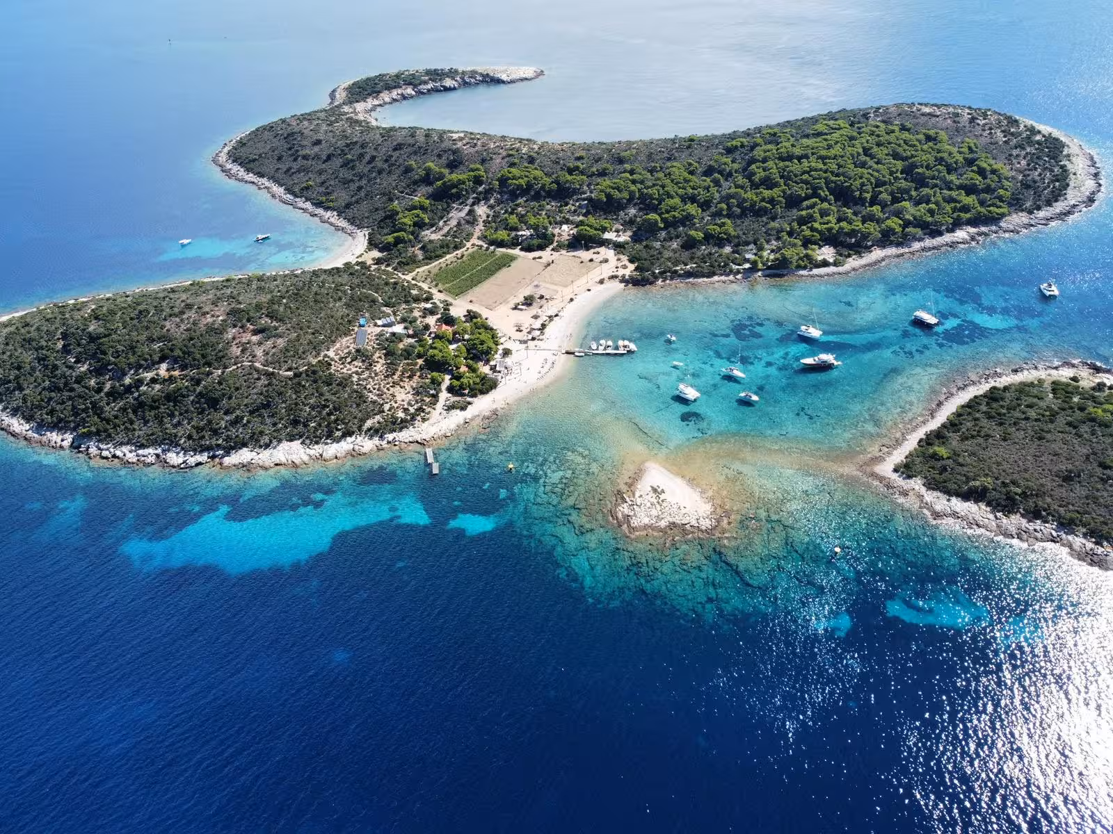 Aerial view of a secluded island bay with yachts in turquoise water, perfect for a sailing adventure cruise