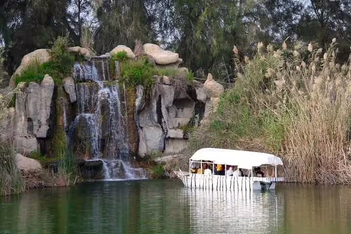 Covered safari boat cruises past a waterfall at Africano Park Alexandria on a private safari tour from Cairo