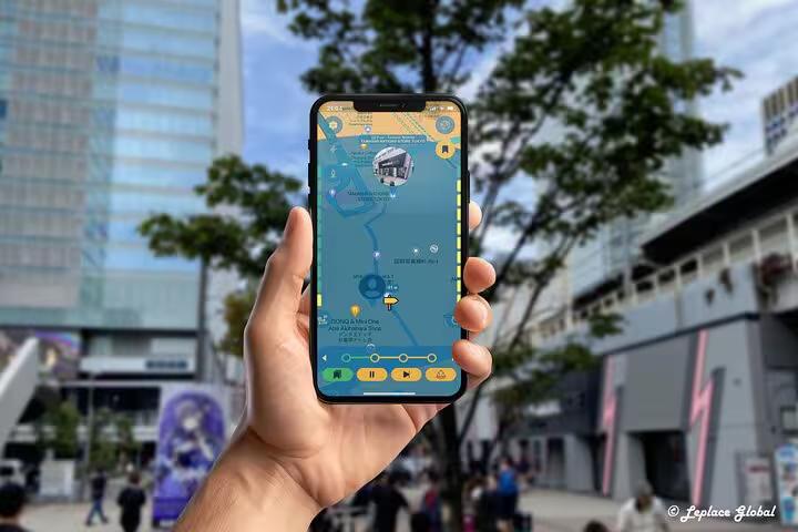 Hand holding smartphone displaying Akihabara walking tour mobile app map with anime buildings in background Tokyo