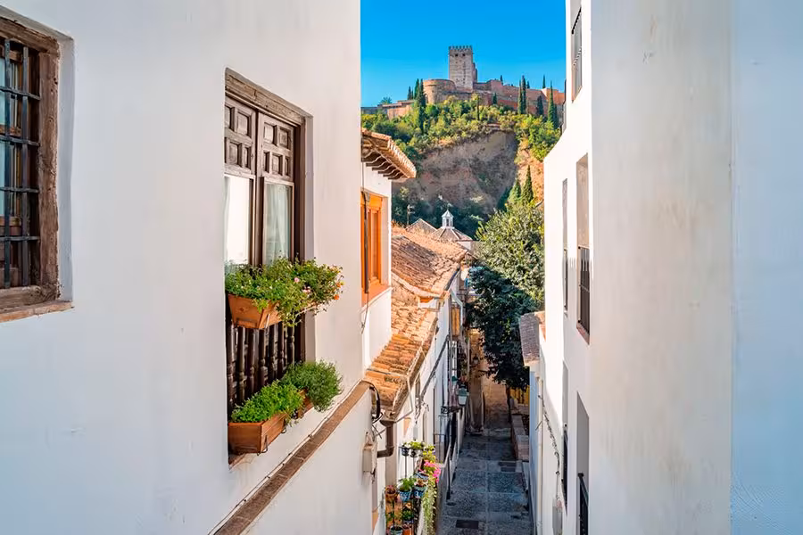 Scenic narrow street in Albaicín with Alhambra view, showcasing traditional Andalusian architecture and flowered balconies.