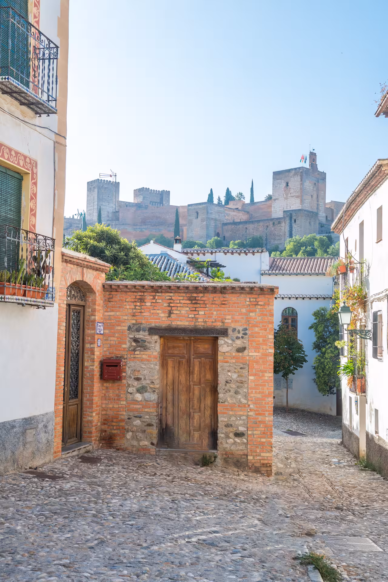 Picturesque Albaicín street with rustic architecture and a stunning view of the Alhambra against a clear sky.