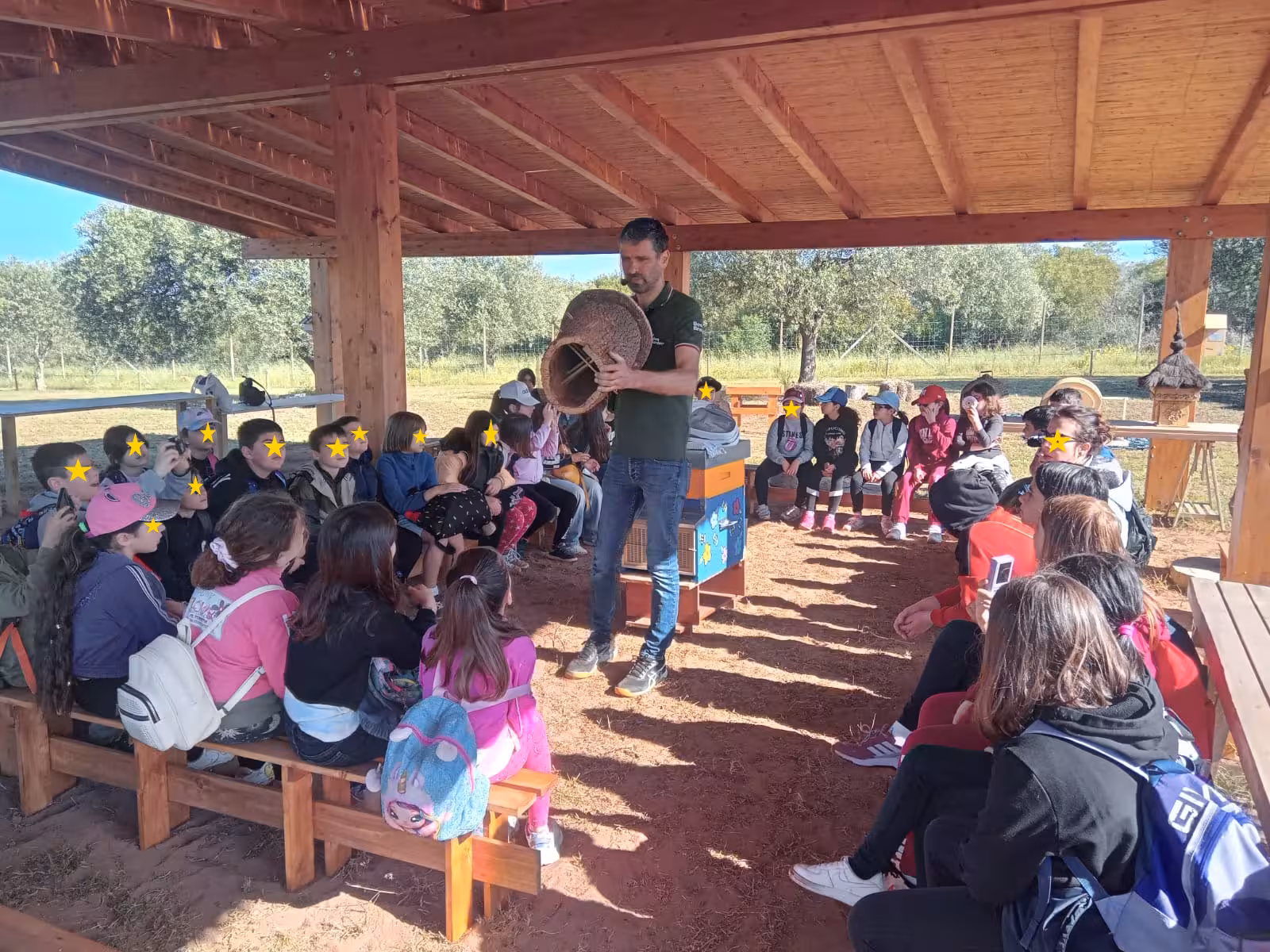 Kids attentively listen to a beekeeper's demonstration in a wooden pavilion at Alghero's bee garden tour in Guardia Grande.