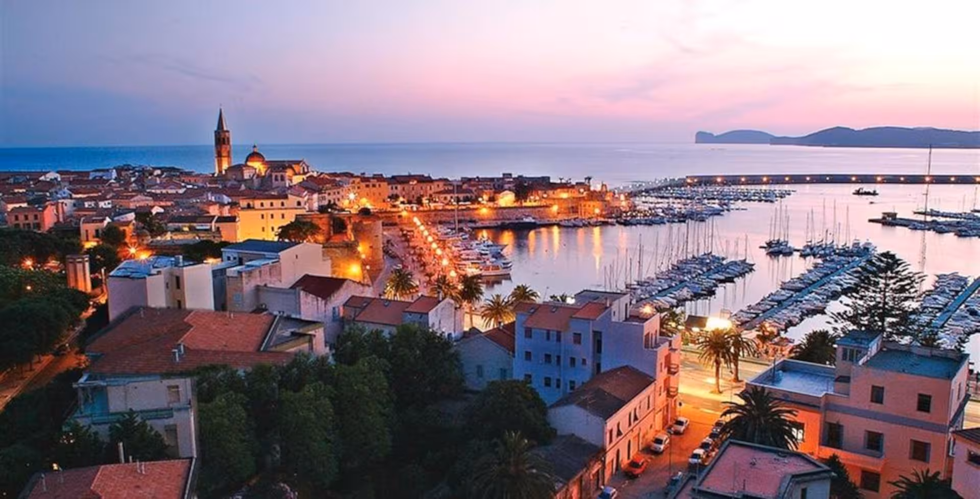 Discover Alghero's charming harbor at sunset, showcasing its historic architecture and serene Mediterranean views.