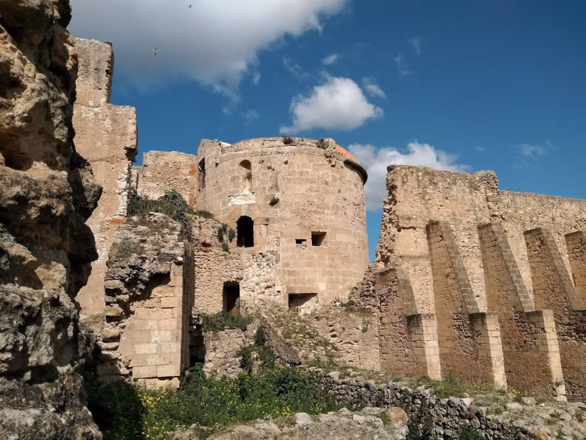 Ancient stone ruins of Alghero's historic centre with a clear blue sky and scattered clouds.