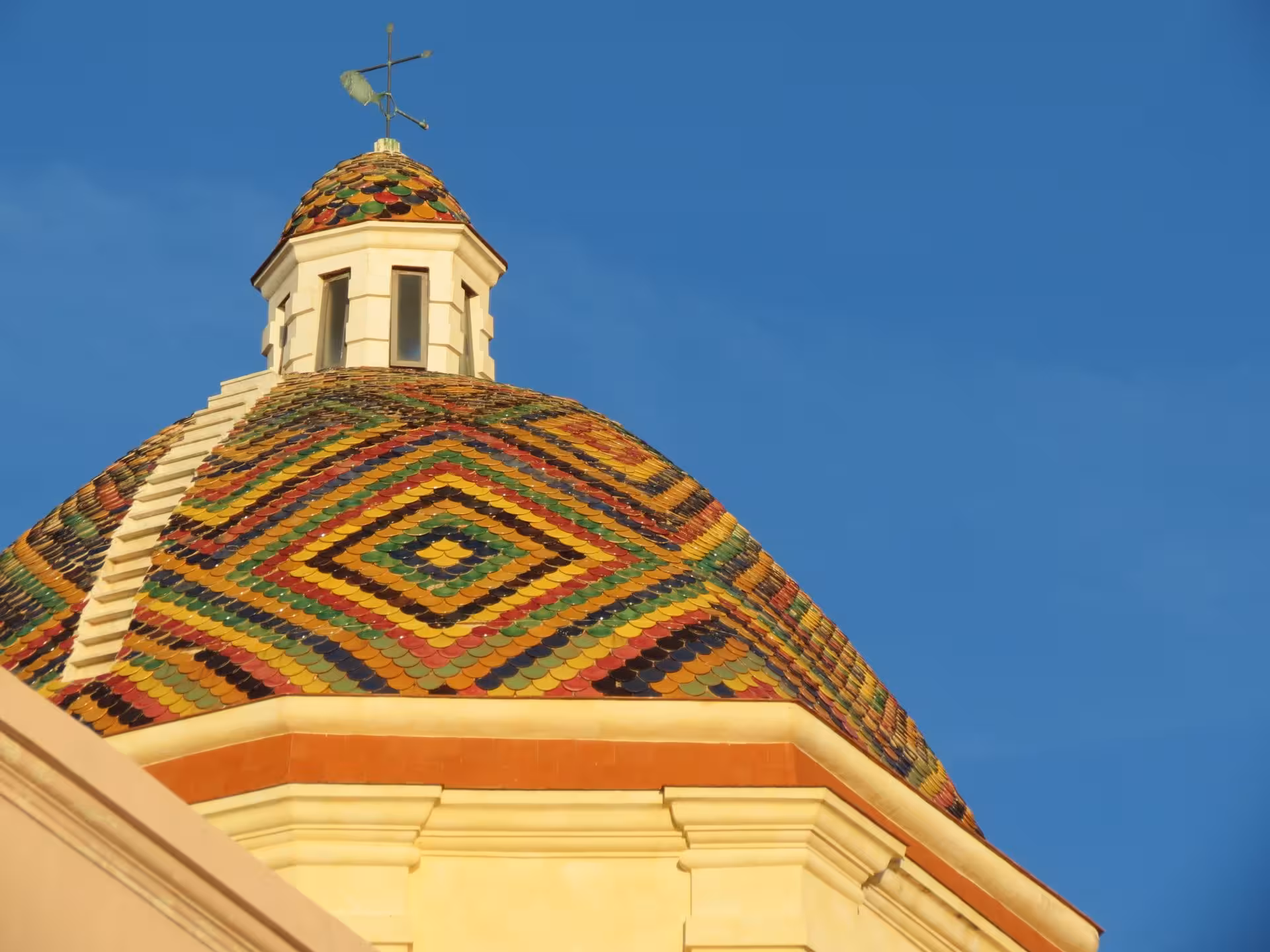 Colorful mosaic dome of Alghero's historic church against a clear blue sky, a highlight of guided tours.