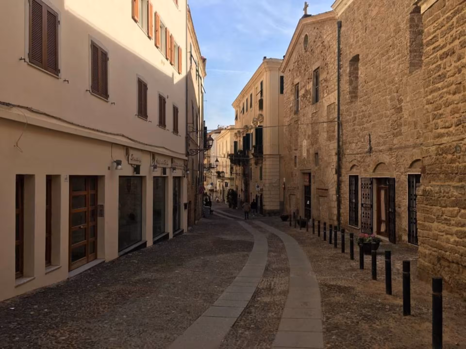 Charming cobblestone street flanked by historic buildings in Alghero's old town, perfect for walking tours.