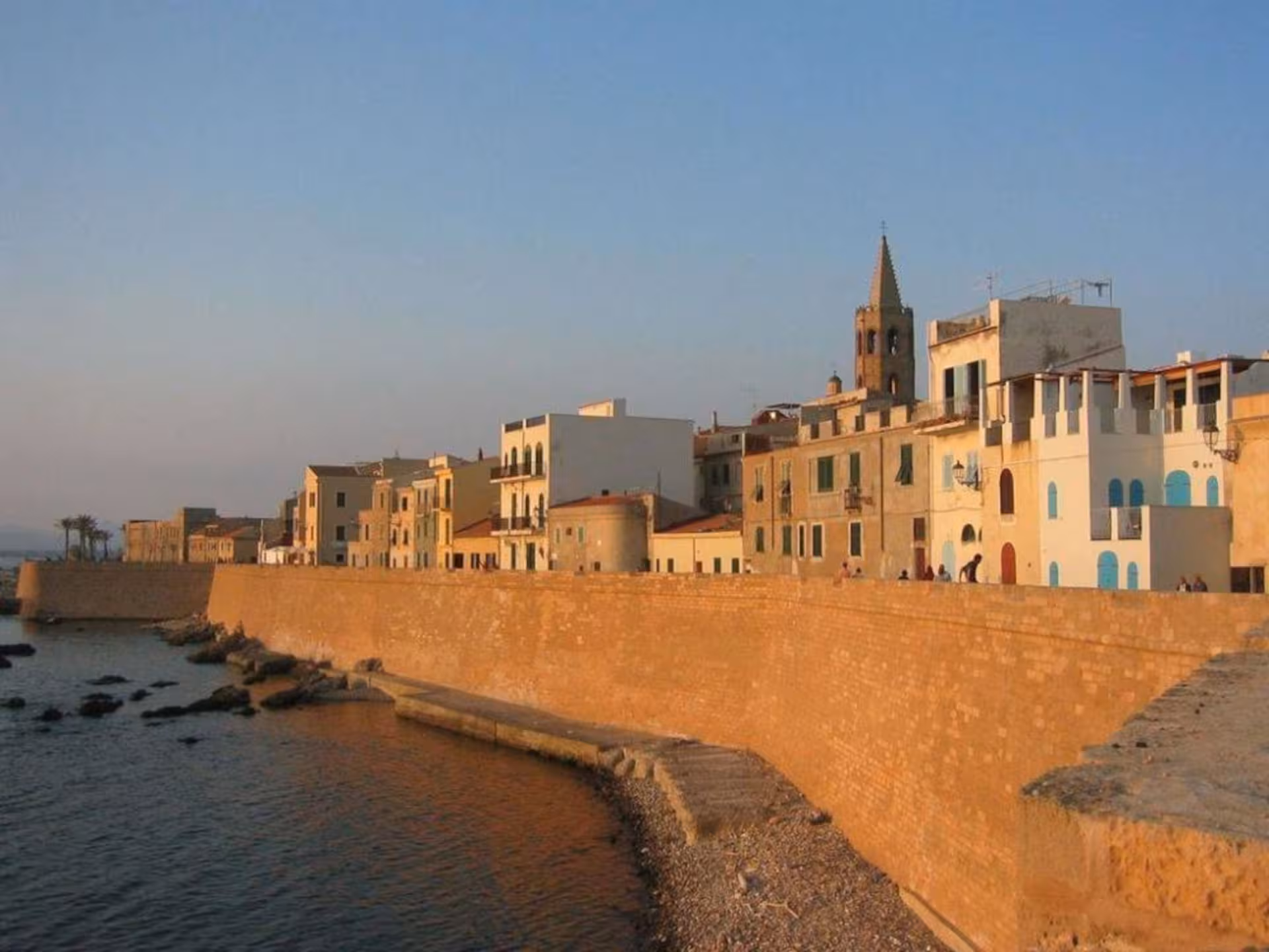 Scenic view of Alghero's historic waterfront and ancient city walls at sunset, ideal for cultural exploration.