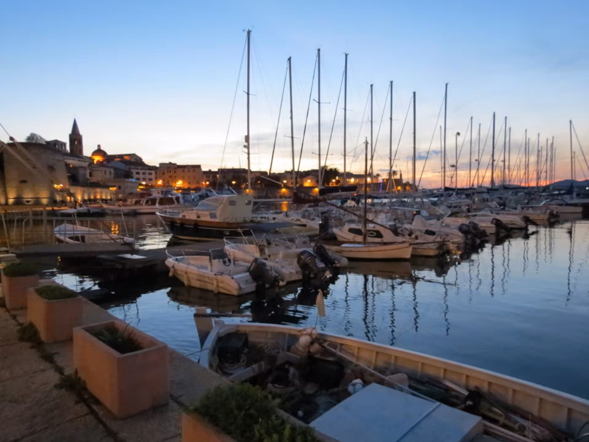 Evening view of Alghero marina with boats reflecting on the water, ideal for a scenic stop on the historic tour.