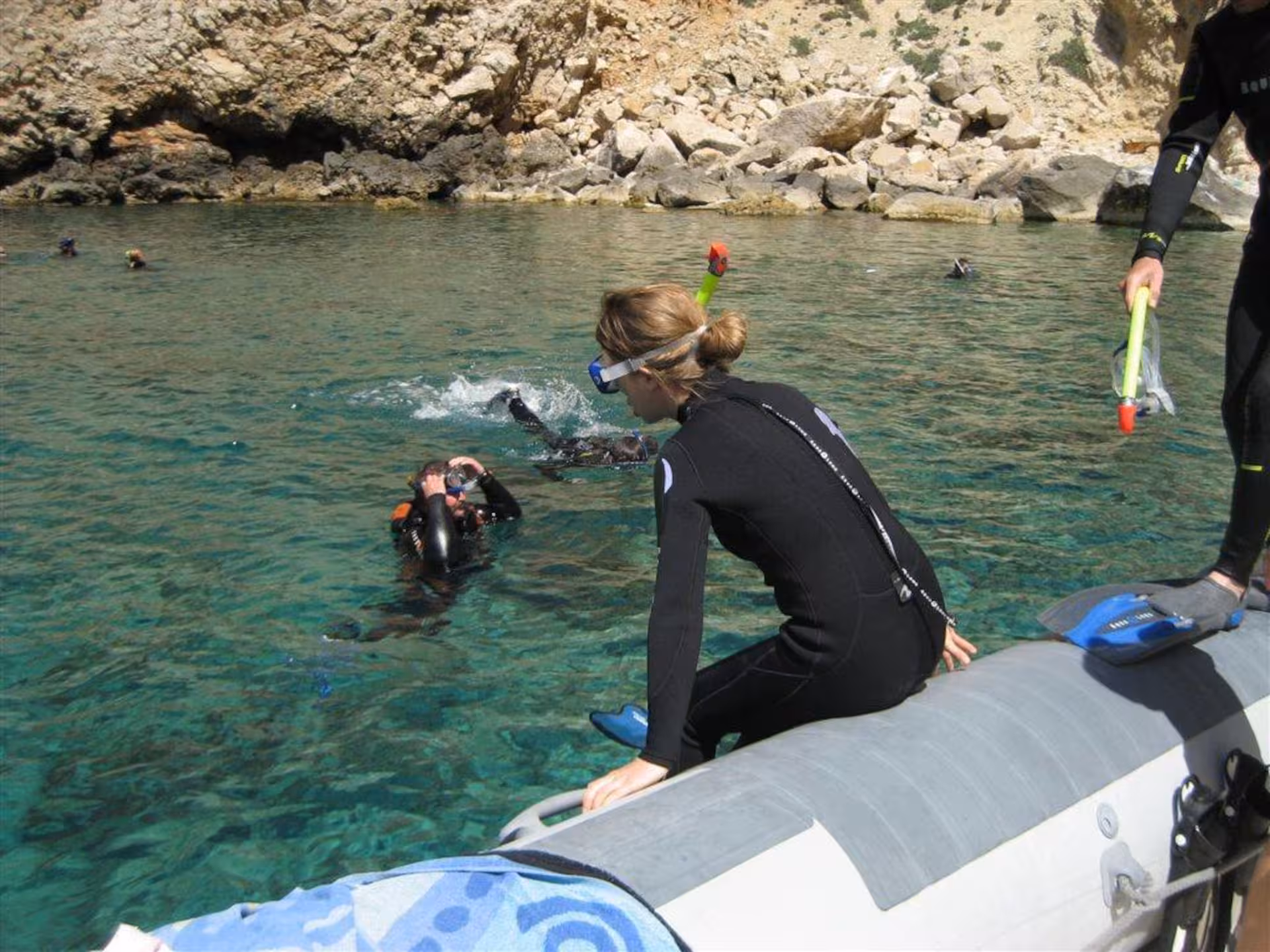 Snorkelers prepare to dive from a boat into the crystal-clear waters of Capo Caccia, Alghero, surrounded by rugged cliffs.