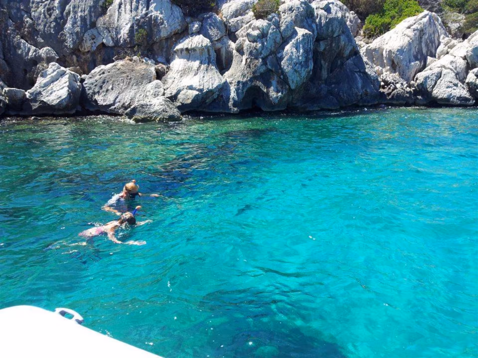 Two snorkelers explore the vibrant turquoise waters along the rocky cliffs of Capo Caccia in Alghero.
