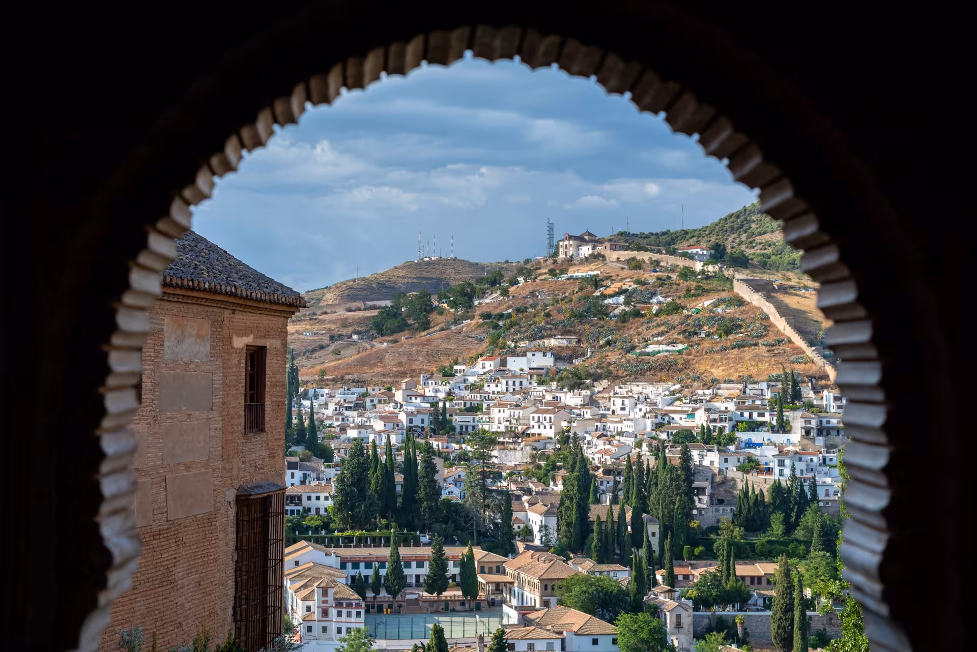 Scenic view of Granada's hillside through an arched window at the Alhambra, offering a glimpse of traditional Spanish architecture.
