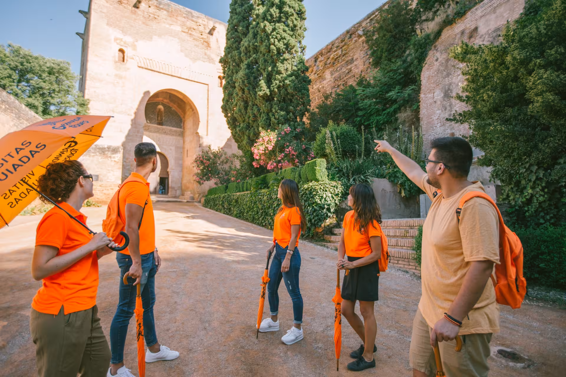 Tour group with guide exploring the ancient gates of the Alhambra, surrounded by lush greenery and historical architecture.