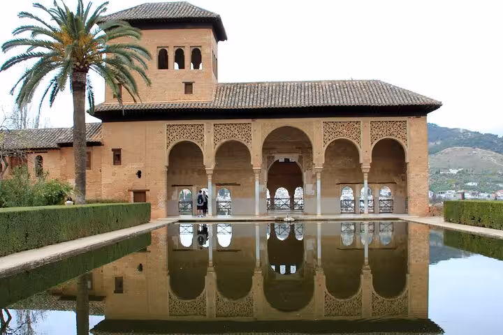 Scenic view of Alhambra's Partal Palace reflecting in a tranquil pool, showcasing Moorish architecture on the Andalusia tour.