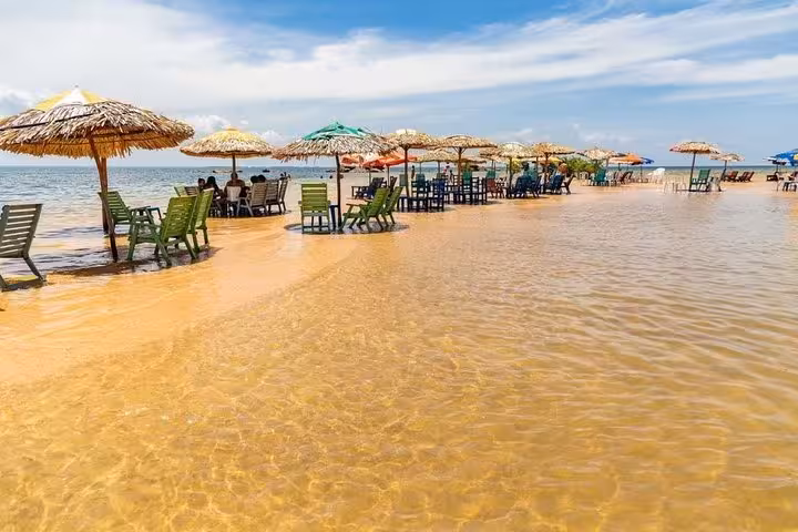 Beach chairs and straw umbrellas in shallow Tapajós River at Alter do Chao, Amazon river beach day tour