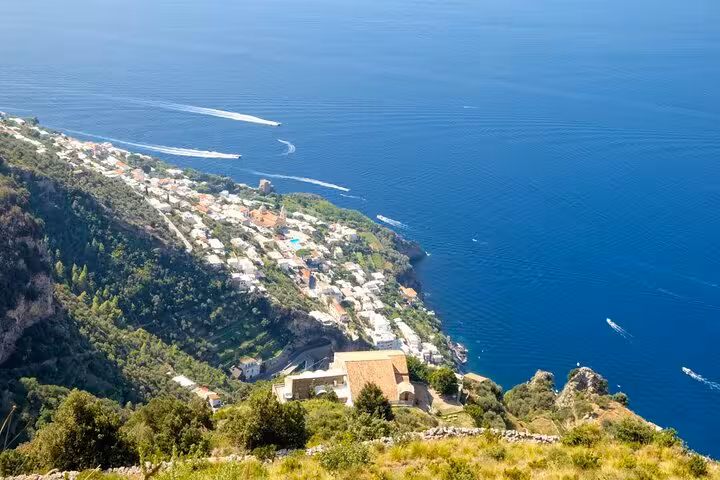 Stunning aerial view of Amalfi Coast's verdant cliffs and azure sea, showcasing picturesque coastal villages and boats.