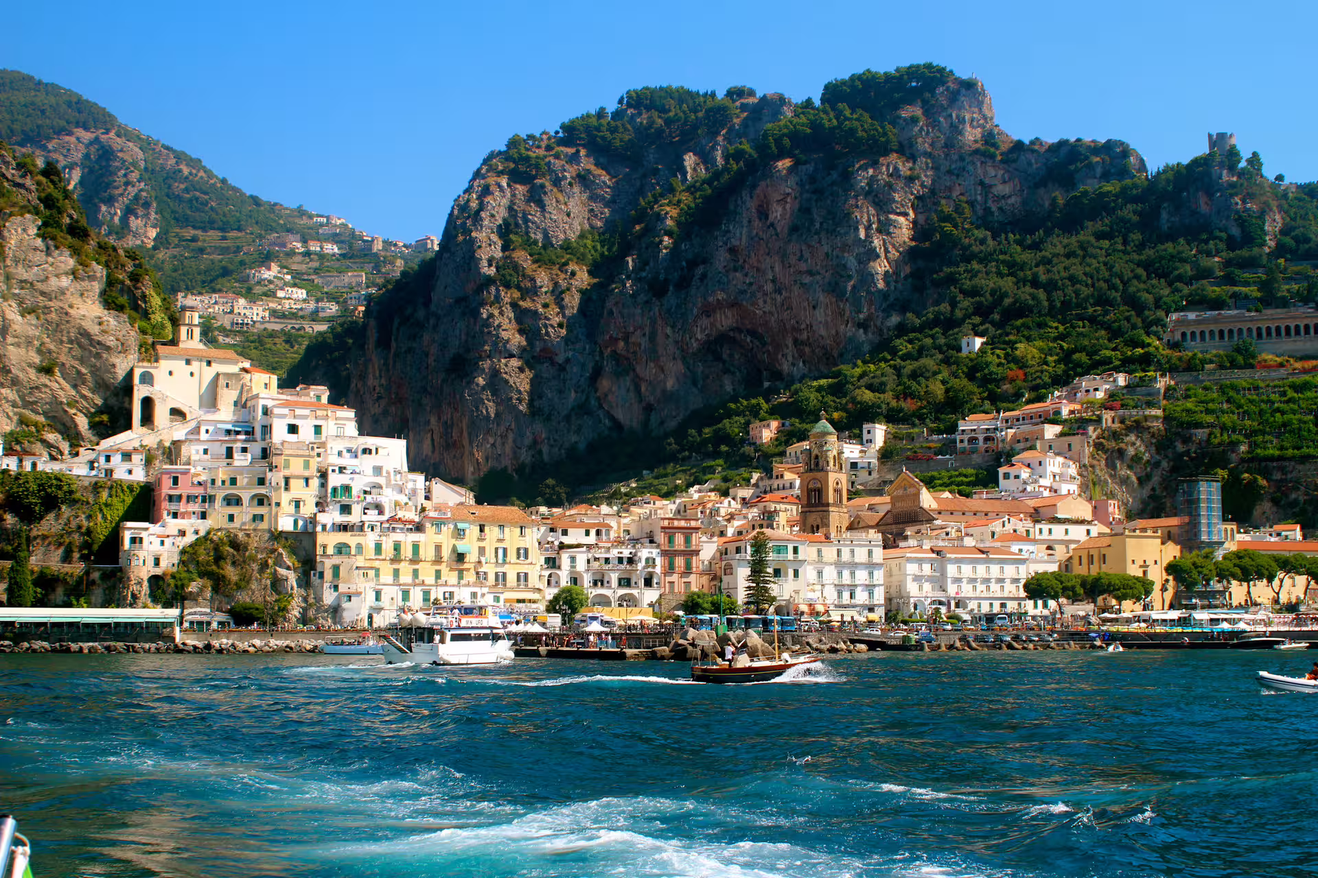 Boats cruising along the Amalfi Coast with pastel seaside village and dramatic cliffs on a Naples and Amalfi Coast tour from Rome