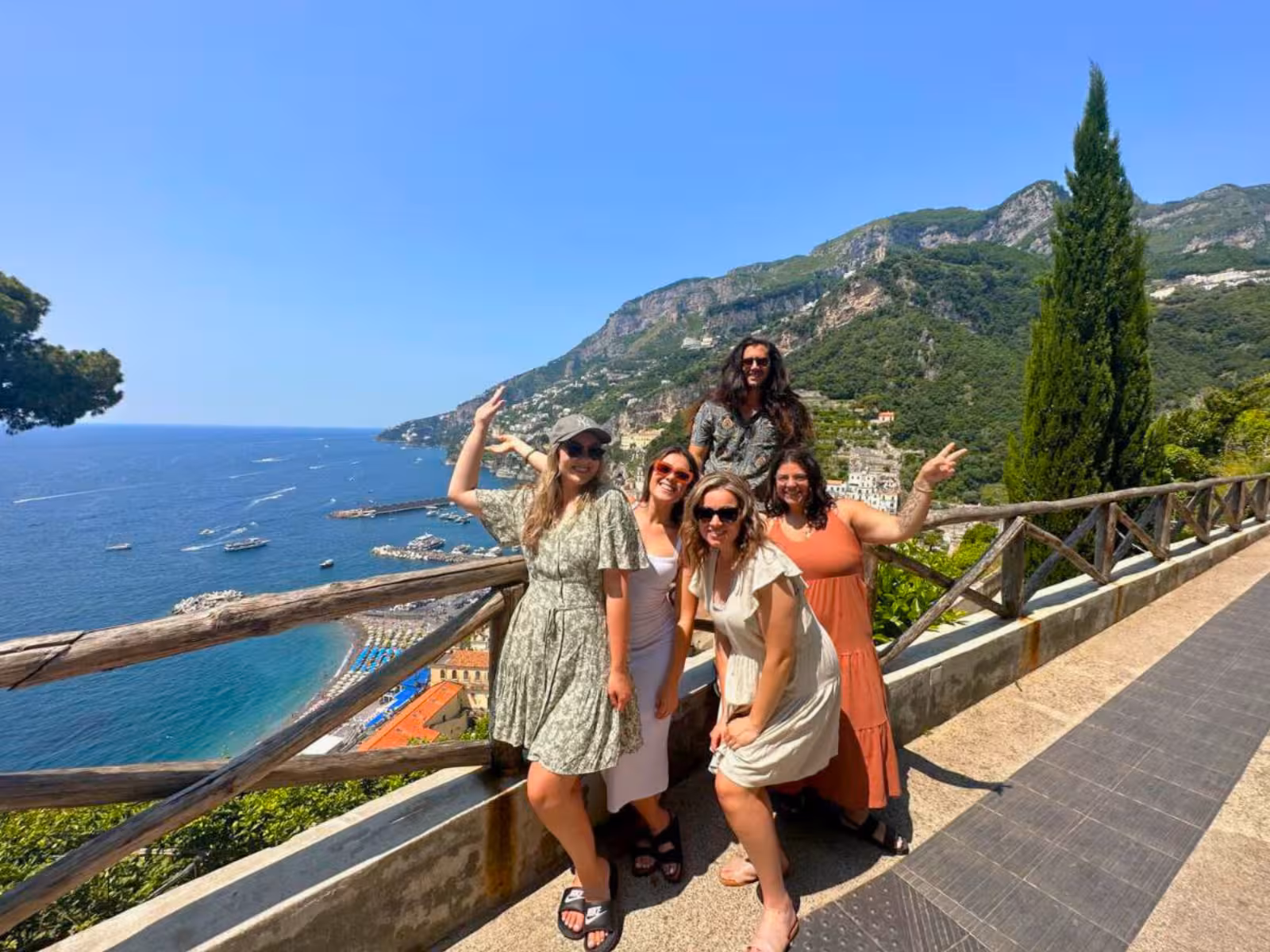 Group of tourists enjoying a scenic view of the Amalfi Coast with clear blue skies and lush green hills.