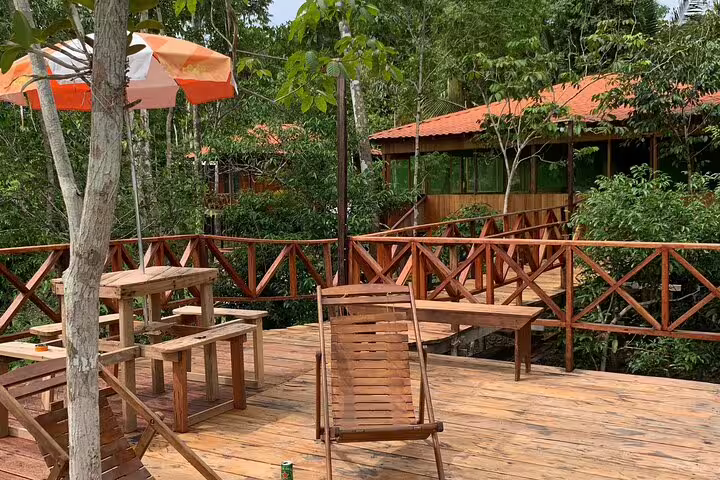Rustic wooden deck with seating overlooks lush Amazon rainforest at Mamori Lodge, offering serene jungle views.