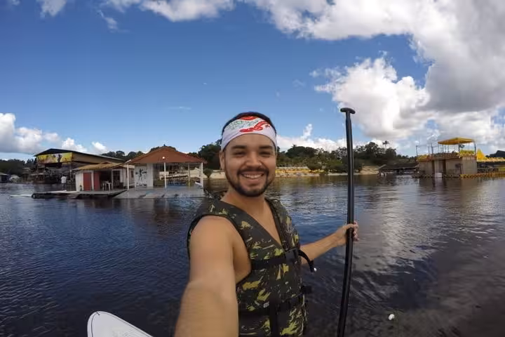 Smiling paddler on Amazon River stand up paddleboard tour near riverside docks under blue sky