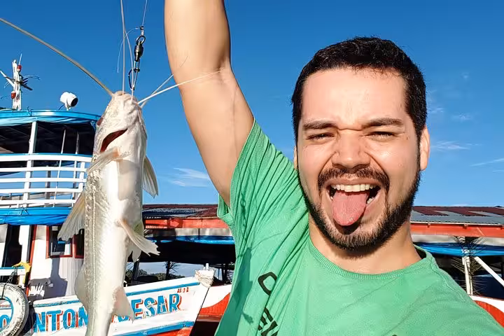 Traveler holding a freshly caught catfish on an Amazon River boat adventure from Manaus, Brazil