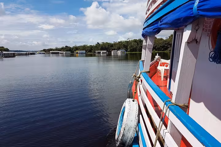 Colorful riverboat cruising calm Amazon waters from Manaus, passing riverside homes on Amazon River adventure